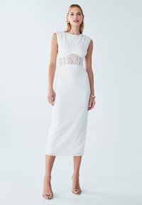 Robe midi en dentelle blanche avec une silhouette ajustée, un col rond et une incrustation en dentelle transparente à la taille. Comprend des manches courtes et une texture lisse.