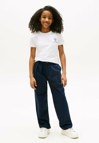 Hvid bomulds-t-shirt med grafisk tryk, parret med marineblå, letvægts bukser med elastisk talje og hvide sneakers.