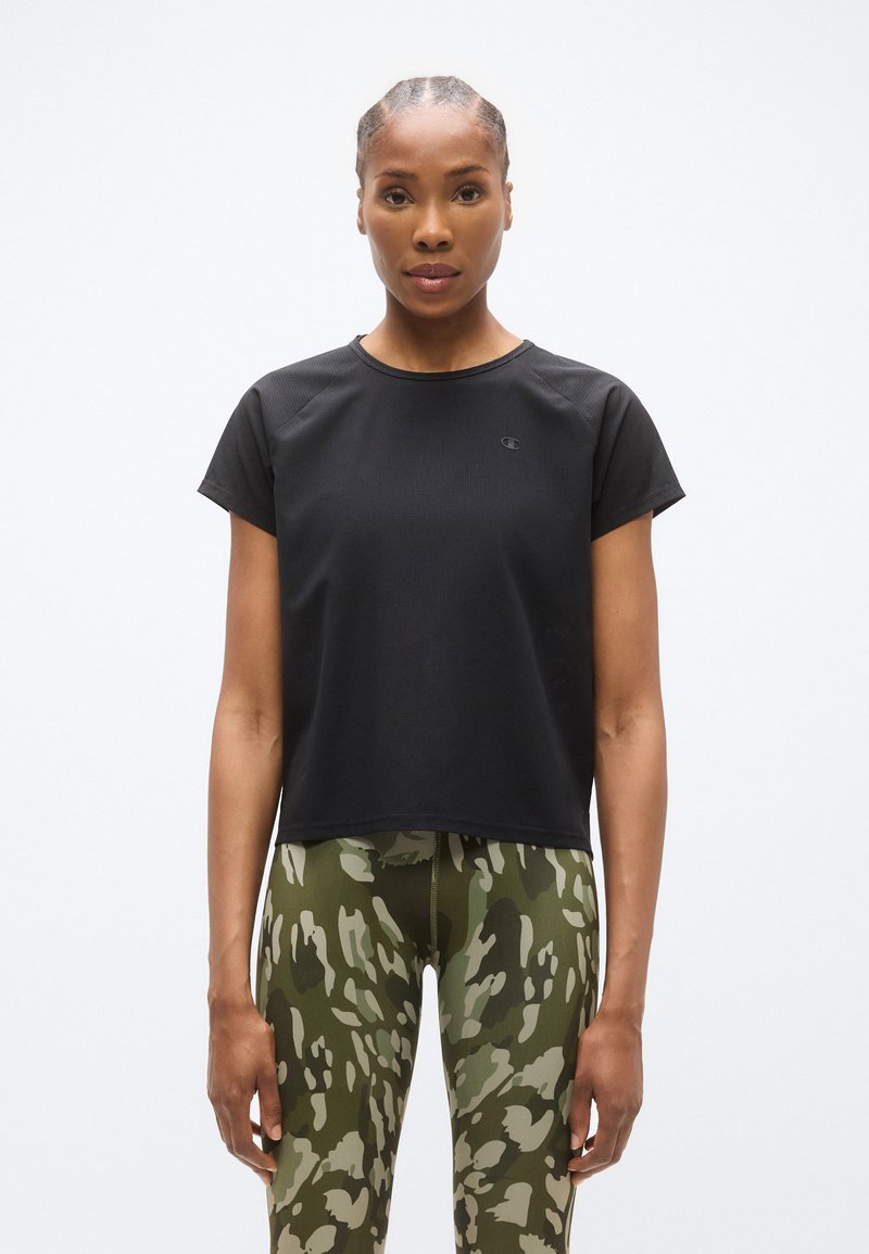 Μαύρο αθλητικό τοπ με κοντά μανίκια, στρογγυλή λαιμόκοψη και υφασμάτινη υφή, συνδυασμένο με πράσινο κολάν καμουφλάζ με εφαρμοστή σχεδίαση.