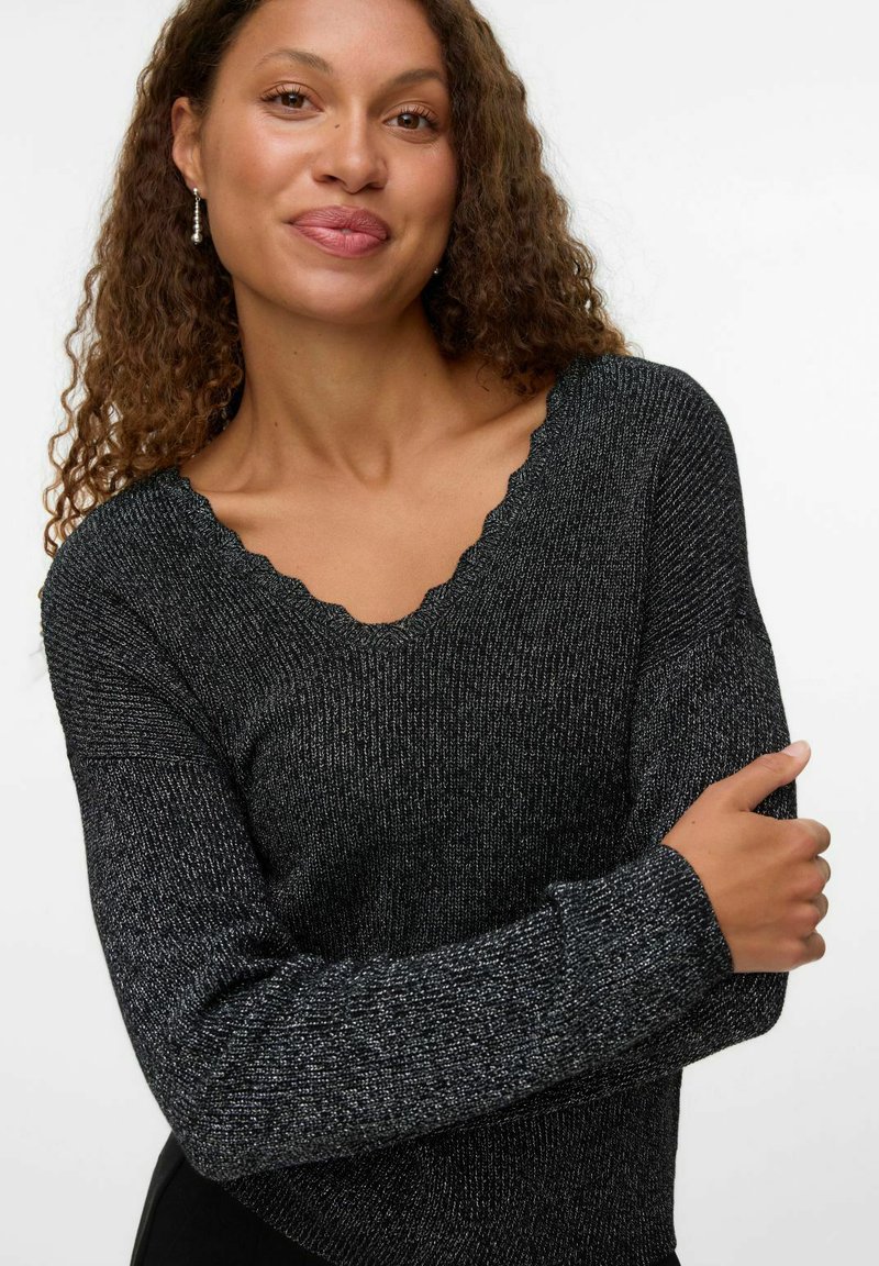 Suéter negro texturizado con escote en forma de V con bordes en picos y mangas largas, confeccionado con un material tejido brillante que añade destellos.