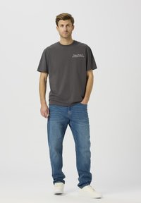 Ciemnoszara bawełniana koszulka z krótkim rękawem, z białym napisem na lewej piersi. W zestawie z niebieskimi dżinsami i białymi trampkami.