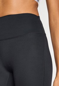 Μαύρα κολάν με ψηλή μέση, κατασκευασμένα από ελαστικό ύφασμα με επίπεδες ραφές, λεία υφή και χωρίς ορατά σχέδια ή διακοσμήσεις.