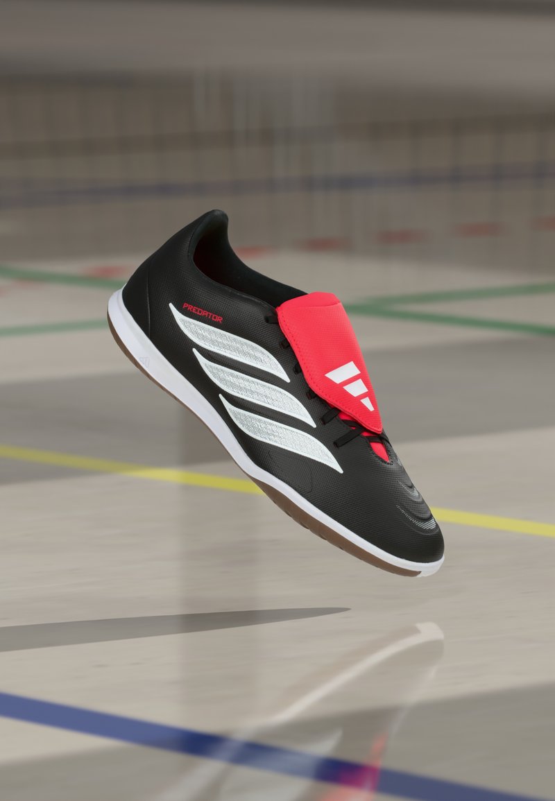 Chaussure de sport noire avec une tige texturée, des accents blancs et une bride rose. Dispose d'une semelle en caoutchouc et d'un logo embossé sur le côté.