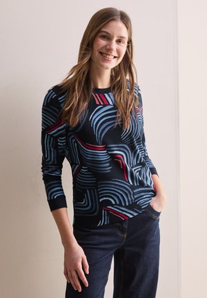 Langsleeve marineblauw top met abstracte blauw-rode gebogen lijnenpatronen. Heeft een ronde hals en fitted manchetten, gecombineerd met donkere jeans.