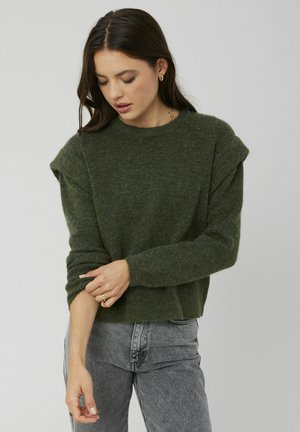 Pull en maille verte avec des épaules tombantes, des poignets côtelés et une coupe décontractée, associé à un jean gris taille haute.