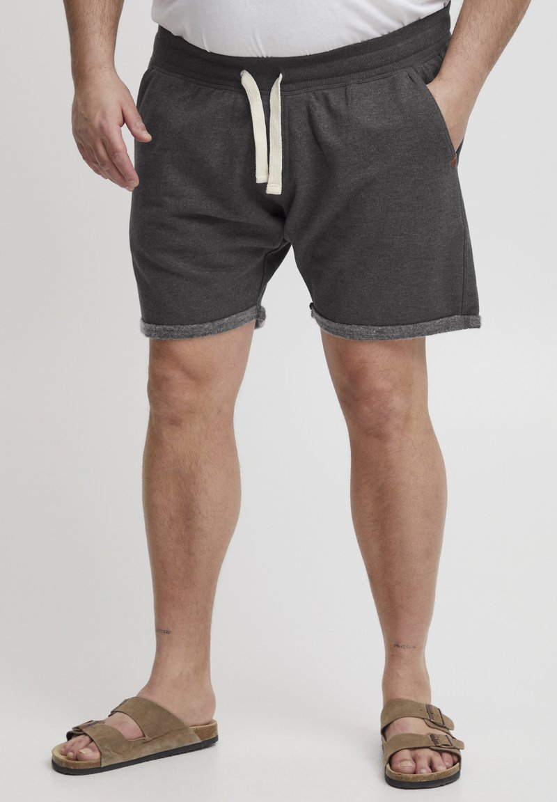Shorts en mélange de coton gris foncé avec une finition ourlée, une taille élastique et un cordon crème, associés à des sandales en daim marron.