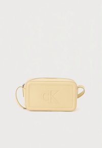 Pochette en cuir jaune de forme rectangulaire, avec un logo "CK" embossé, une fermeture éclair et une poignée latérale pour un transport facile.