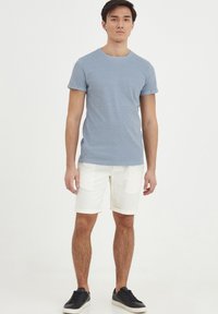 Svetlo modré tričko s krátkym rukávom z jemného materiálu; kombinované s bielymi ľanovými šortkami s vyhrnutým rukávom; nosené s čiernymi teniskami.