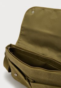 Χιαστί τσάντα ώμου σε ελιά πράσινη από ανθεκτικό ύφασμα, με φερμουάρ, μαγνητικό κλείσιμο και λιτό σχεδιασμό.