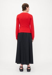 Pull rouge ajusté avec des manches longues, associé à une jupe midi noire. Présente un ourlet côtelé et une texture lisse, porté avec des chaussures noires épaisses.
