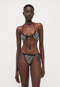 Čierny bikiny set s trojuholníkovým vrchom a spodnými nohavičkami na viazanie, ozdobený striebornými aplikáciami. Hladká tkanina s lesklým povrchom.