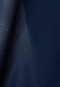 Donkerblauwe stof met een gestructureerd patroon, gekenmerkt door kleine, reflecterende stippen die een gradiënt effect creëren van donker naar licht.
