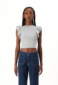 Un top scurt gri cu dungi, cu mâneci volan, asociat cu blugi din denim închis la culoare, cu talie înaltă, prevăzuți cu închidere prin buton și buzunare spate.