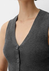 Grå, ribbat, ärmlös kardarigan med djup V-hals och två svarta knappar framtill, med en strukturerad tygutseende.