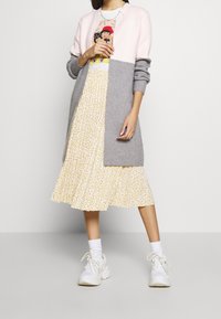 Szaro-różowy kardigan w stylu color-block nałożony na żółtą kwiecistą sukienkę, w połączeniu z białymi trampkami. Sukienka ma zwiewny, plisowany fason.