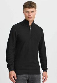Sweater noir à col zippé, doté d'un motif tricoté texturé, de poignets et d'un ourlet côtelés, ainsi que d'un col haut pour plus de chaleur.