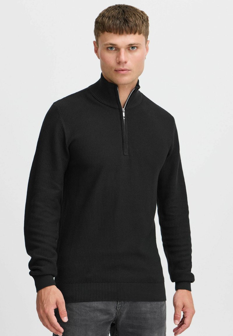 Sweater noir à col zippé, doté d'un motif tricoté texturé, de poignets et d'un ourlet côtelés, ainsi que d'un col haut pour plus de chaleur.