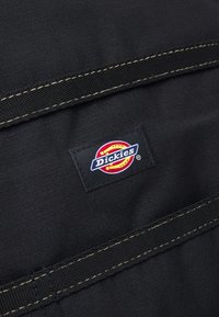 Fekete szövet folt színes "Dickies" logóval, vörös, sárga és kék díszítéssel. Kiemelkedik egyszerű, tartós dizájnjával és varrásával.