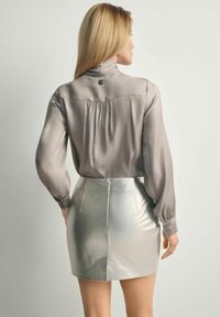 Jasnoszara bluzka z długim rękawem i wysokim kołnierzem, w połączeniu z metalicznie srebrną mini spódnicą z tylnym zamkiem błyskawicznym i detalami w plisach.