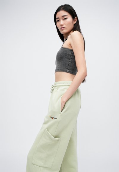 Sivý rebrovaný crop top v kombinácii so svetlozelenými teplákmi s vyšitým dizajnom a bočnou kapsou. Jednoduchý, moderný strih.