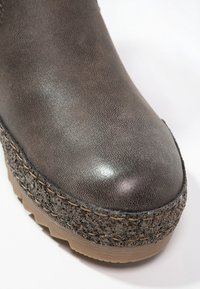 Bottine en synthétique grise avec un dessus lisse, semelle plateforme texturée avec des accents mouchetés et des détails cousus le long du bord.