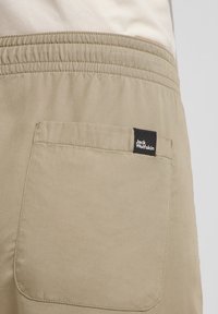 Beige stoffen shorts met een elastische tailleband. Beschikt over een achterzak met een zwart Jack Wolfskin-label. Gladde textuur, eenvoudig ontwerp.
