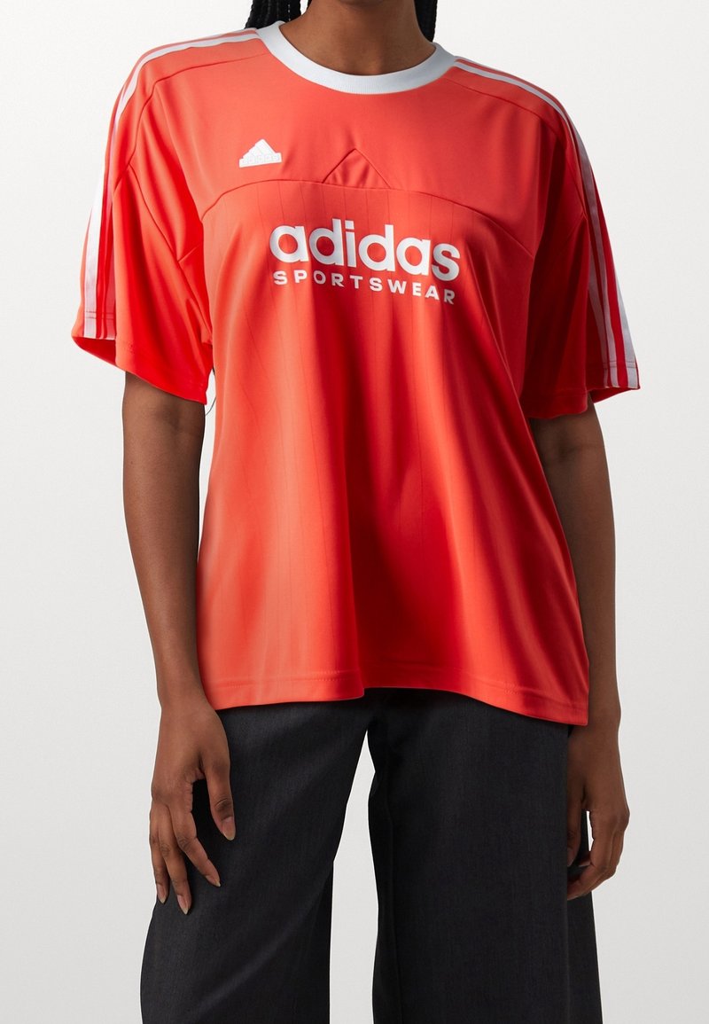 Červené sportovní tričko Adidas s bílým logem a třemi pruhy. Krátké rukávy, kulatý výstřih, lehký materiál, hladká textura, volný střih.
