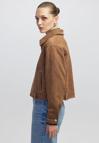 Veste courte en velours côtelé marron avec des accents en studs argentés le long du col et des poches, dotée d'une fermeture éclair et de détails en bouton.