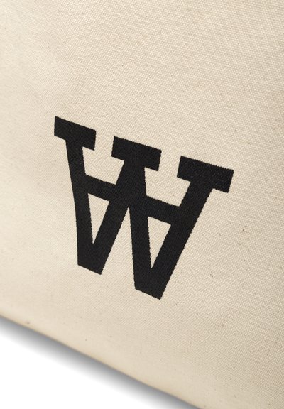 Sac en toile avec un extérieur beige arborant un grand logo noir en "W" inversé. Tissu durable et design minimaliste.