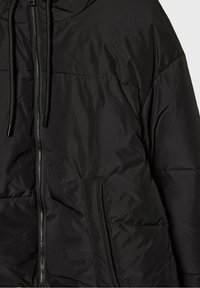 Doudoune noire avec fermeture éclair frontale, capuche avec cordons de serrage et poches latérales diagonales, présentant une texture matelassée lisse et cousue.