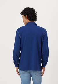 Polo majica s dugimi rukavi v temno modri barvi. Mehak material s ovratnikom, diskretnimi šivi in ravnim robom. Minimalističen dizajn.