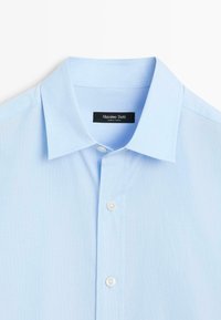 Světle modrá košile s límcem a jemnou texturou, se šesti knoflíky na předním zapínání a štítkem s nápisem "Massimo Dutti."