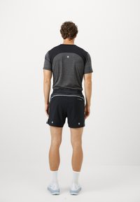 Grå og svart treningsskjorte med korte ermer, parret med svarte shorts med reflekterende detaljer og en myk, lett tekstur.