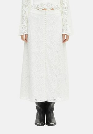 Witte kanten midi-rok met knopen aan de achterkant, gedragen met een bijpassend kanten top en zwarte Western-stijl laarzen.
