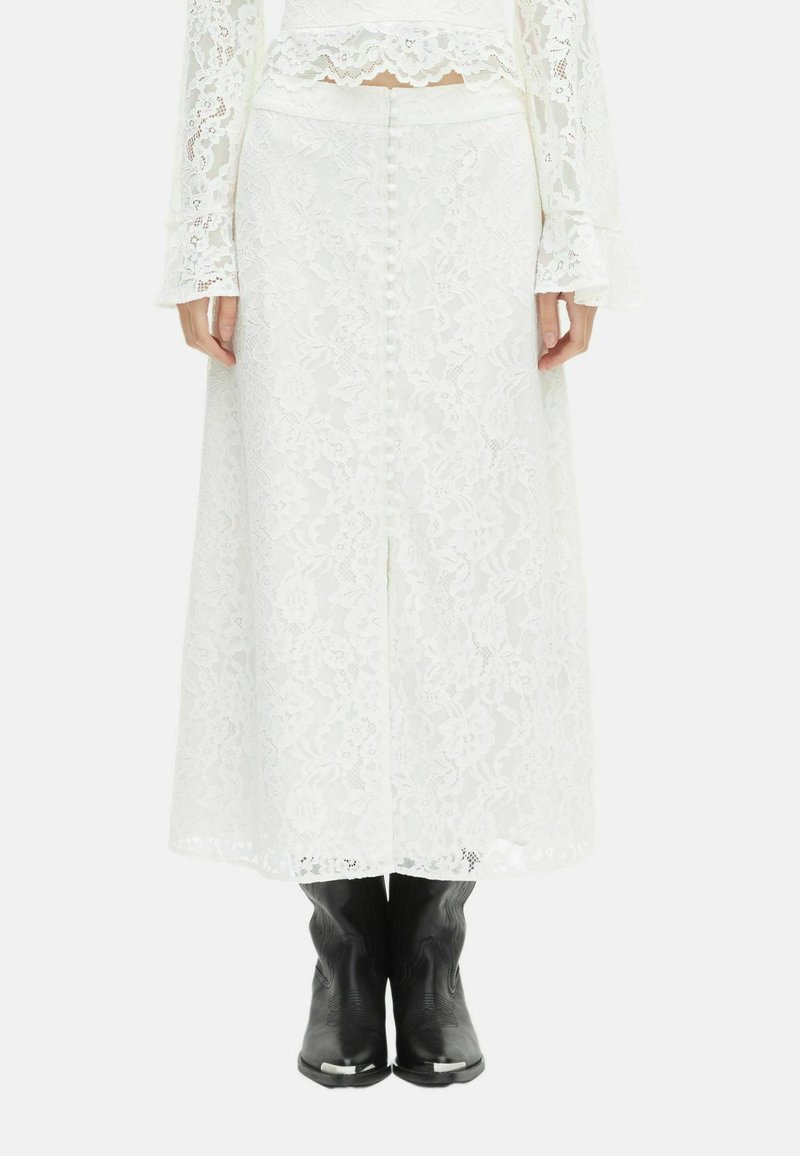Witte kanten midi-rok met knopen aan de achterkant, gedragen met een bijpassend kanten top en zwarte Western-stijl laarzen.