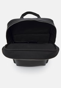 Mochila negra con una abertura con cremallera, que cuenta con un interior suave, múltiples compartimentos y un asa resistente en la parte superior para un fácil transporte.