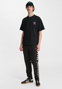 Zwarte katoenen t-shirt met een kleine kleurrijke graphic op de linkerborst, gecombineerd met zwarte joggingsbroek met witte zigzagstrepen aan de zijkanten.