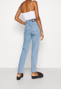 Džíny s vyšším pasem z modrého denimu s zúženými nohavicemi a dvěma zadními kapsami, ve spojení s bílou tílkovou košilí a černými platformovými sandály.