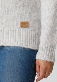 Light gray knitted sweater with a ribbed hem, featuring a leather tag labeled "SWEDEMOUNT." Soft texture and loose fit.