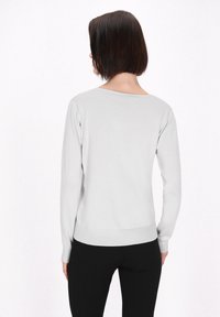 Heller grauer Langarmpullover mit rundem Halsausschnitt und geripptem Saum. Weicher Stoff und schlanker Schnitt. Getragen mit schwarzen Hosen.