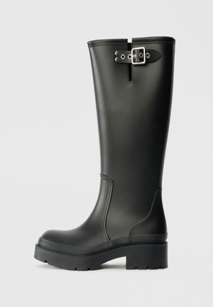 Crne čizme do koljena s debelim đonom i detaljem od srebrne kopče pri vrhu, prikazane sa strane na jednostavnoj pozadini.