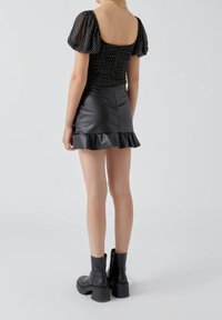 Schwarzes Oberteil mit Puffärmeln und weißen Punkten, kombiniert mit einem schwarzen Minirock aus Kunstleder mit Rüschen, ergänzt durch klobige schwarze Stiefeletten.