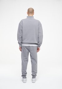 Suéter gris y pantalones de chándal a juego en una suave tela cepillada; corte relajado; cuello alto; puños acanalados; llevados con una camiseta blanca por debajo y calzado.