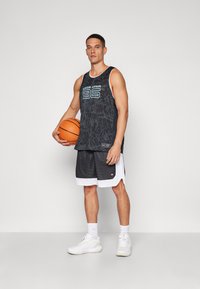 Zwarte mesh basketbalsjersey met teal accenten en grafisch ontwerp, gecombineerd met zwarte shorts met witte bies en witte sportchoenen.
