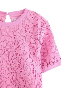 Vaaleanpunainen lyhythihainen mekko, jossa on kukkakuvioinen pitsiyhteys ja pyöreä pääntie, varustettuna nappisuljennalla avonaista selkää varten.