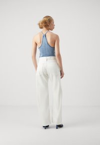 Top halter de mezclilla en azul claro combinado con pantalones anchos blancos. El atuendo presenta un diseño simple y acentos minimalistas.