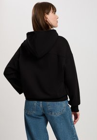 Czarna bluza z kapturem o luźnym kroju, wykonana z grubego materiału, z prążkowanymi mankietami. Noszona z jasnoniebieskimi spodniami o wysokim stan. 