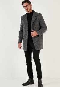 Abrigo de patrón en blanco y negro con cuello muesca, cierre de botones y bolsillos laterales, llevado sobre un cuello alto negro y pantalones negros ajustados.