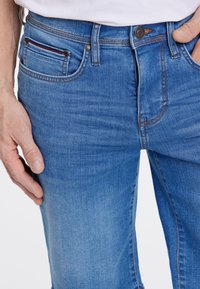 Siniset farkut suoralla lahkeella, joissa on napitus, kuparinväriset ompeleet ja etutaskut koristeellisella trimmauksella.