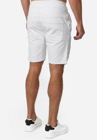 Pantalones cortos de mezclilla blanca con un detalle deshilachado en el lateral, dos bolsillos traseros y una cintura elástica, combinados con zapatillas blancas con acentos negros.